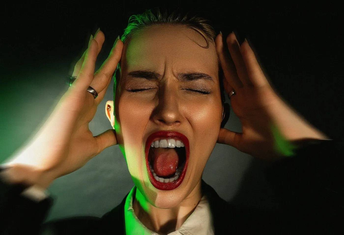 Woman with eyes closed and mouth open in a scream, holding her temples